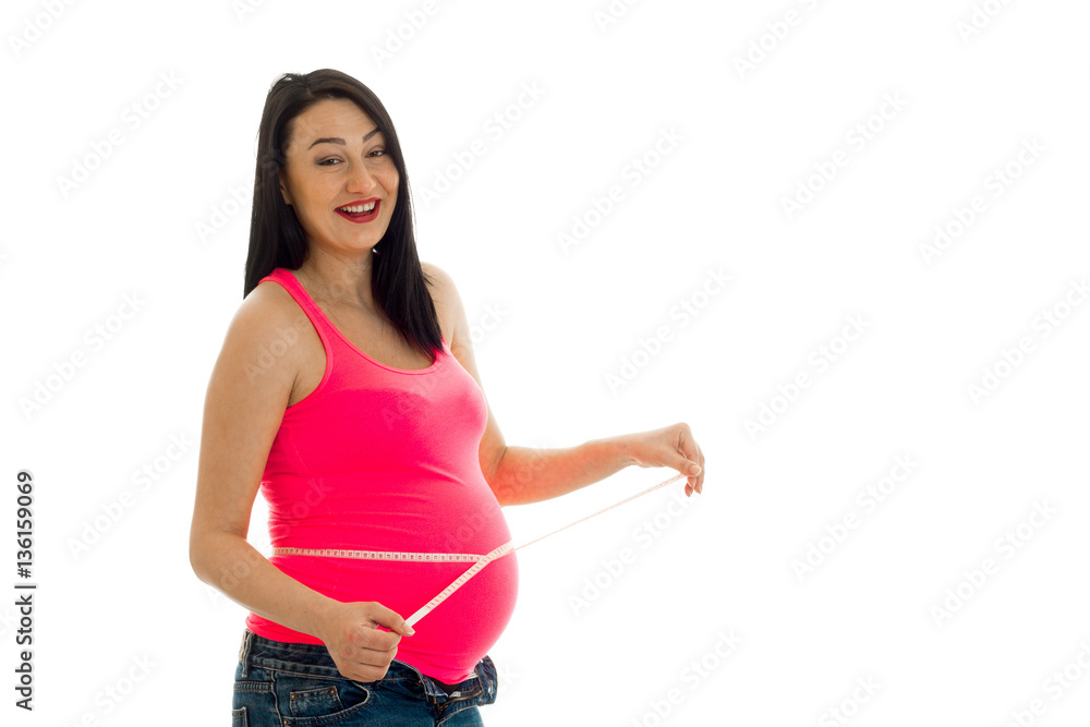 Young cheerful pregnant mother laughing and measure her belly isolated on white background in studio Young cheerful pregnant mother laughing and measure her belly isolated on white background in studio