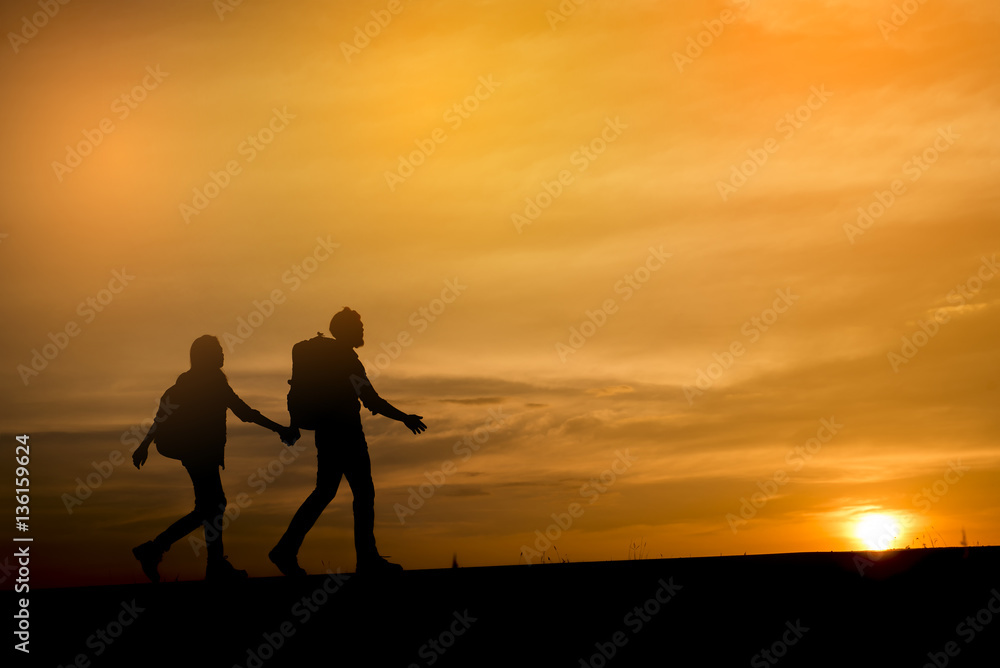 Silhouette of two backpackers (man and woman) who were traveling.The background image is a sunset in Thailand.Man and woman are walking hand in hand.