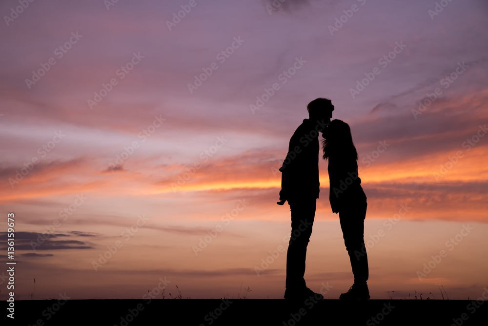 Silhouette of lovers standing hug and kiss.The background image is a sunset in Thailand.