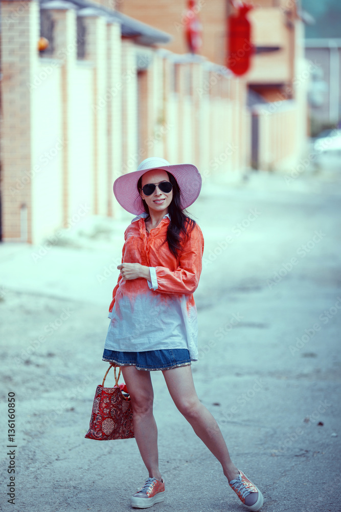 Beautiful young woman in elegant hat and sunglasses posing outdo
