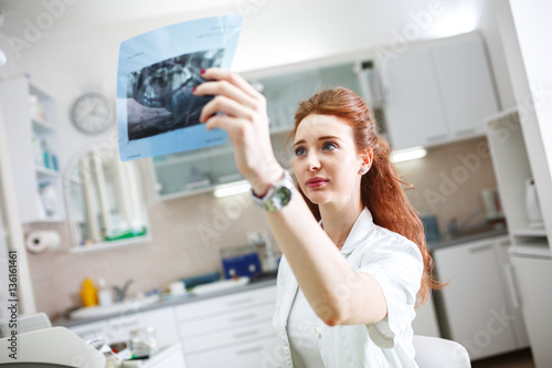 Female red hair dentist in dental office examining x-ray image.