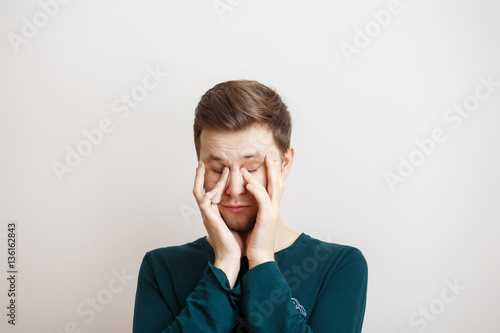 Sleepy young man rubbing eyes on a light background