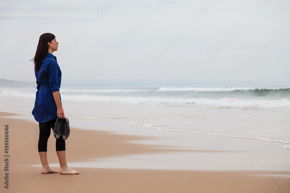 Lonely and depressed woman watching the sea in a deserted beach on an Autumn day.