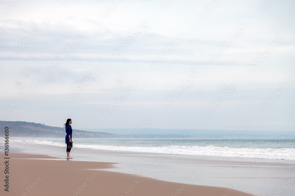 Lonely and depressed woman watching the sea in a deserted beach on an Autumn day.