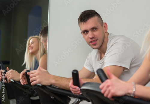 Young man and woman biking in the gym, exercising legs doing cardio workout cycling bikes