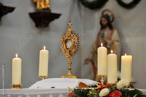 Obraz na plátně Monstrance and four white candles on the altar with Jesus' statue in the background