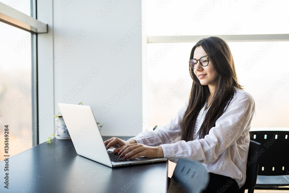 young woman worker sitting in office while using laptop computer and typing by keyboard young woman worker sitting in office while using laptop computer and typing by keyboard