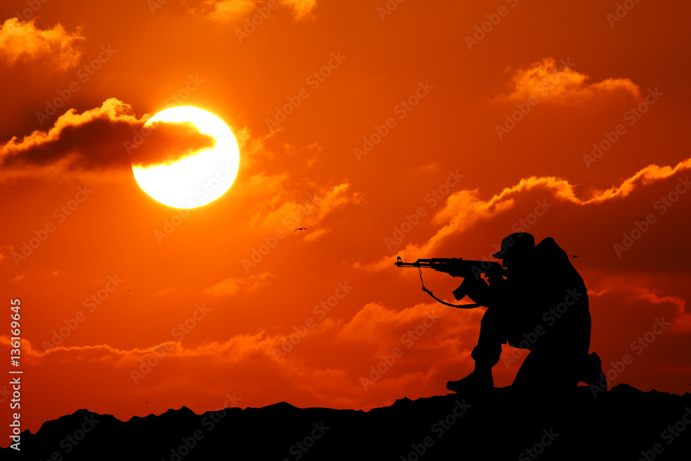 Silhouette shot of a soldier holding a gun with a picturesque mountain backdrop at sunset