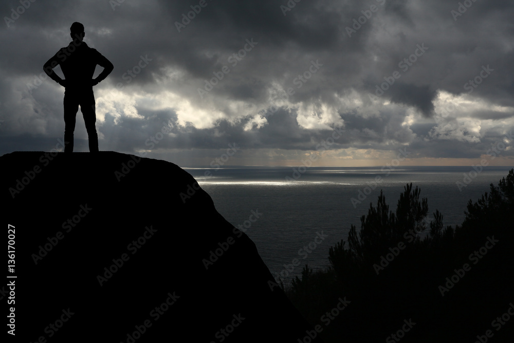 man against the sea standing on a mountain top looking into the distance man against the sea standing on a mountain top looking into the distance