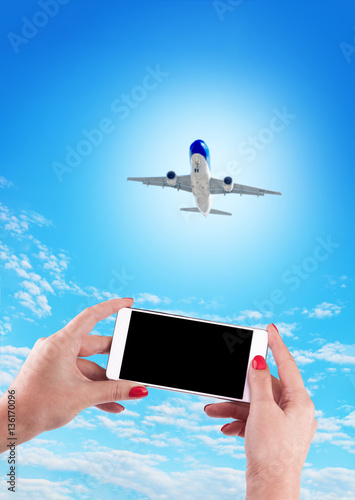 Female Hand holding using mobile phone and airplane on a blue ba