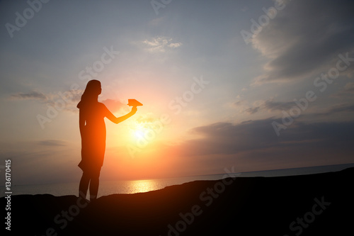 silhouette of a girl at sunset let a paper plane