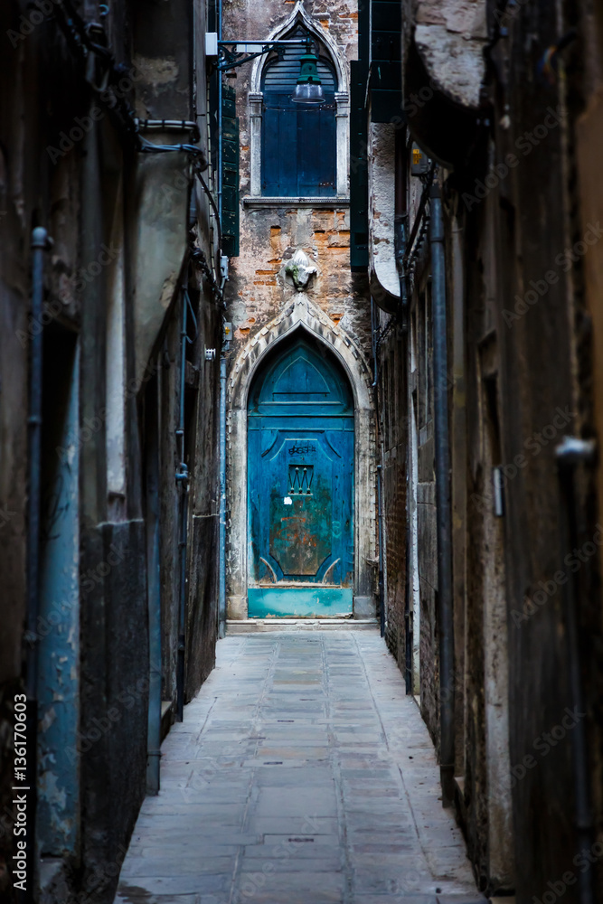 Narrow street and picturesque medieval door among old brick houses in Venice. Veneto, Italy