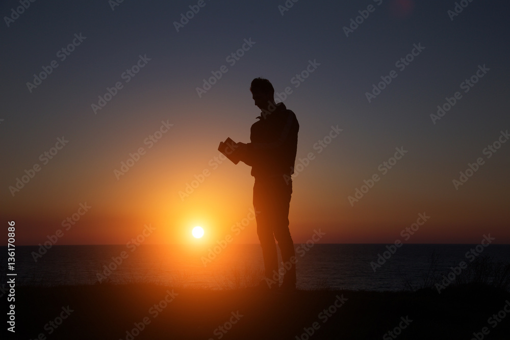 man reading an interesting book on the background of a beautiful sunset