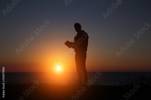 man reading an interesting book on the background of a beautiful sunset © YURII Seleznov