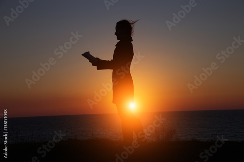 silhouette of a girl reading an interesting book on the background of a beautiful sunset