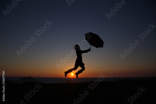 silhouette of a girl with an umbrella at sunset jumping