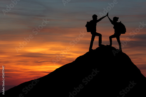 Male and female hikers climbing up mountain cliff and one of them giving helping hand. People helping and, team work concept.