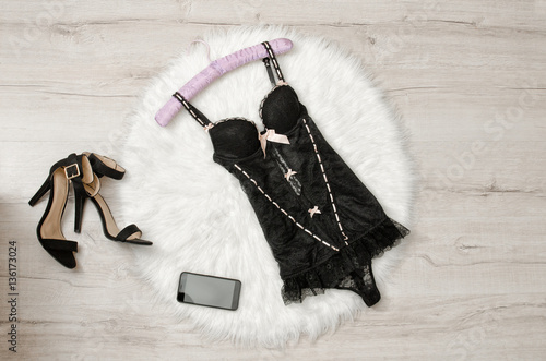 Black lace corset, shoes and smart phone on a white fur. Fashionable concept, top view