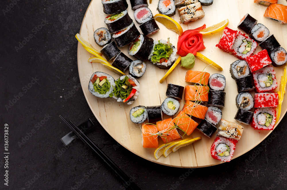 Japanese cuisine. Sushi set on a round wooden board over black concrete background.