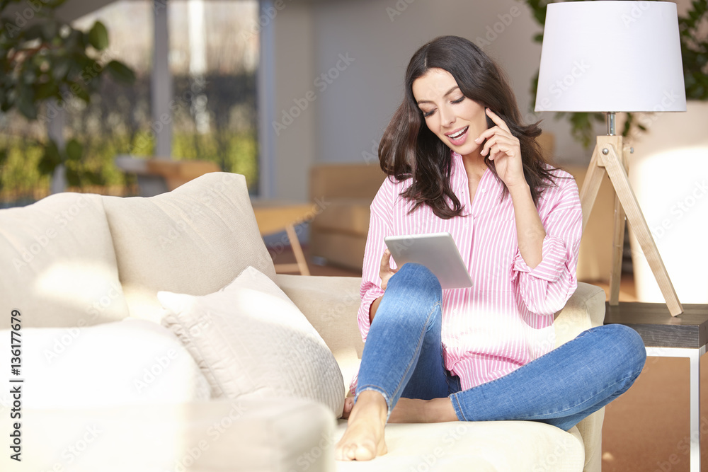 Browsing on the internet. Full length shot of a young woman using her digital tablet while sitting in her cozy home. Browsing on the internet. Full length shot of a young woman using her digital tablet while sitting in her cozy home.