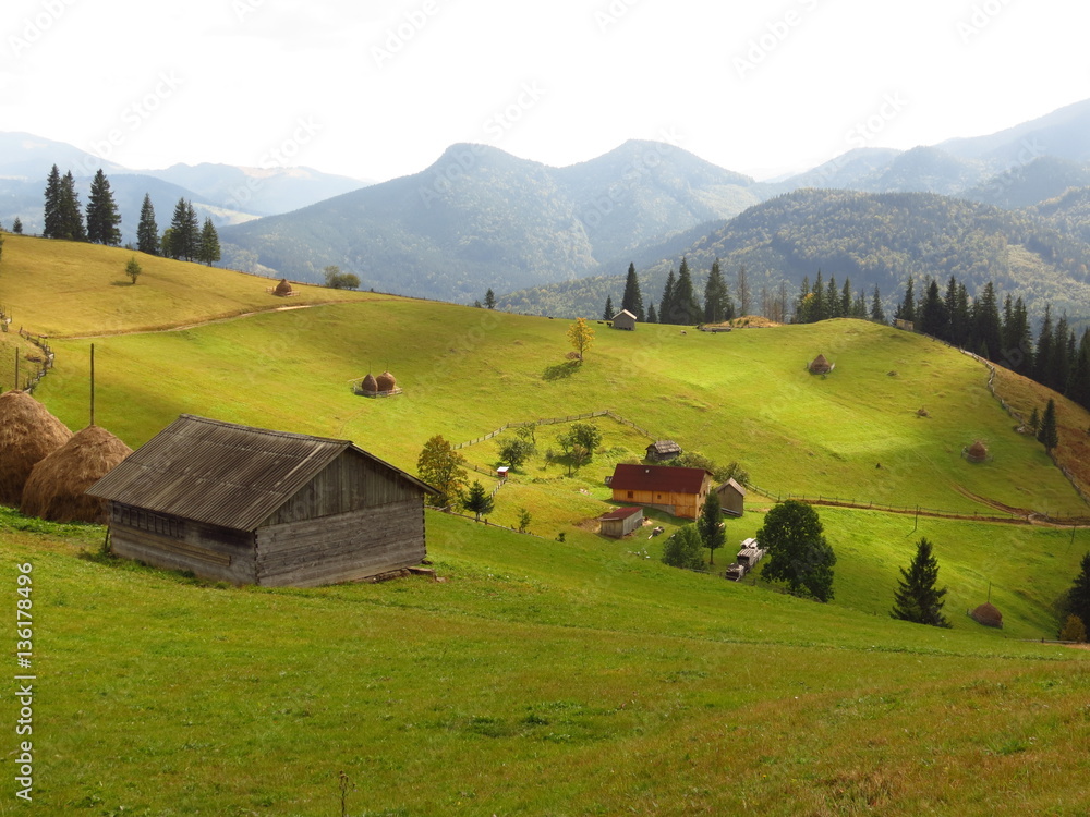 Old wooden hut and haystacks on  background of  beautiful mountain landscape and clouds.