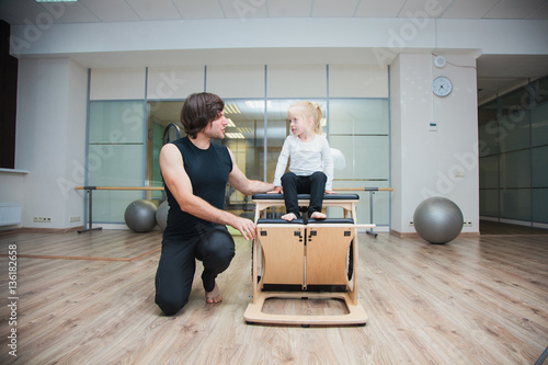Pilates coach training child using special equipment. 