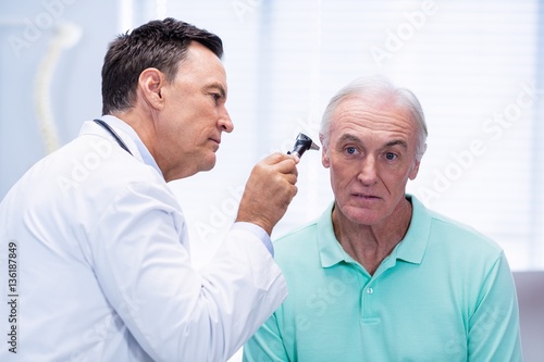 Doctor examining patients ear with otoscope photo