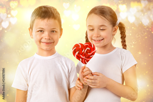 Boy gives a little girl candy red lollipop in heart shape. Valentine's day. Kids love.