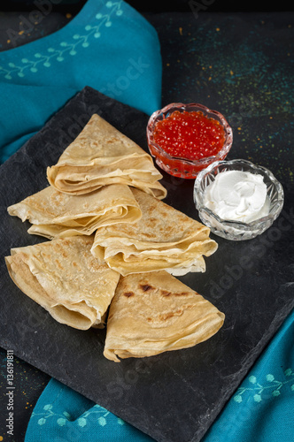 Russian pancake blini with fresh cream and red caviar on dark ba photo