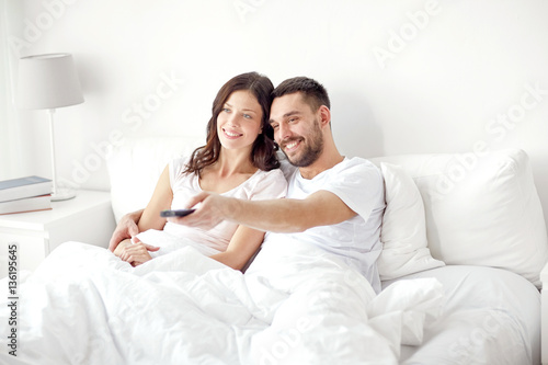 happy couple lying in bed at home and watching tv