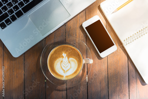 Top view coffee notebook cell phone and laptop on wood table vintage tone.