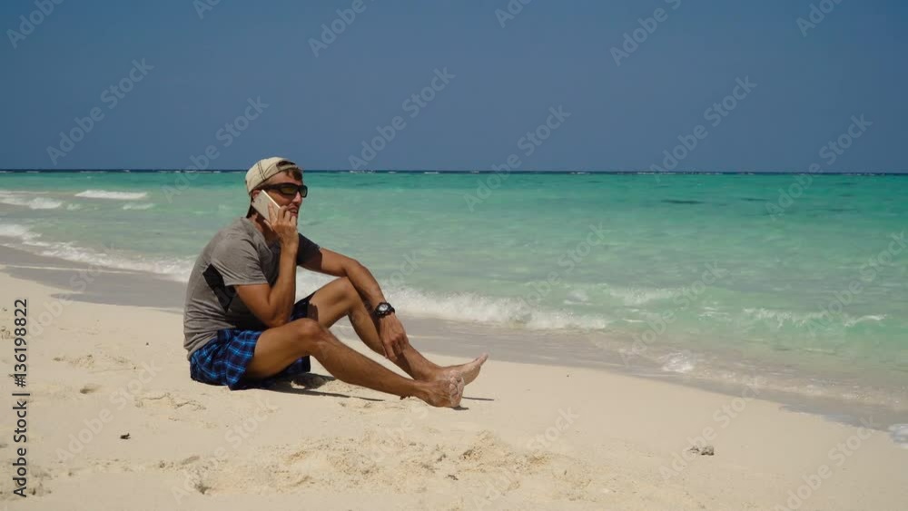 Man talking on the mobile phone at the beach. Man talking on cell phone and sitting along beach. Beach, sea, sand,wave. Philippines, Travel concept. 4K video Man talking on the mobile phone at the beach. Man talking on cell phone and sitting along beach. Beach, sea, sand,wave. Philippines, Travel concept. 4K video