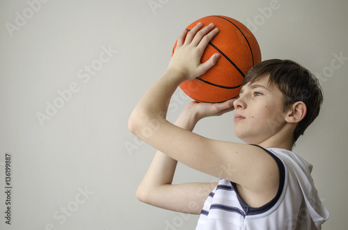 Teenager boy in a white shirt with a ball for basketball on a light background   © vomirak