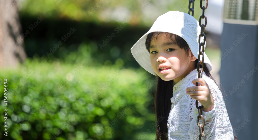 Beautiful little girl sitting on a suspended swing in the park in summer Beautiful little girl sitting on a suspended swing in the park in summer