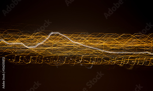 Abstract of an array of horizontal gold lines with one white light running through it on a black background