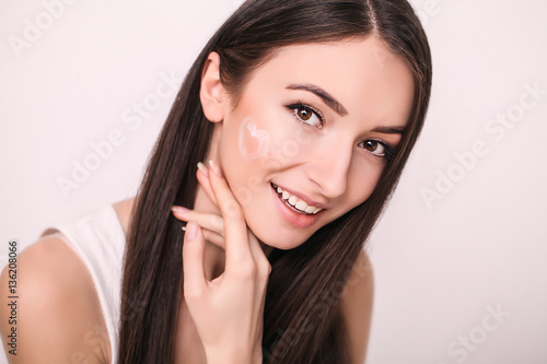 Face Treatment. Woman in Beauty Salon. Applying cosmetic cream. A beautiful young woman applying face moisturizer. Scine care of the face and hands