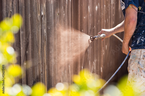 Professional Painter Spraying House Yard Fence with Wood Stain.