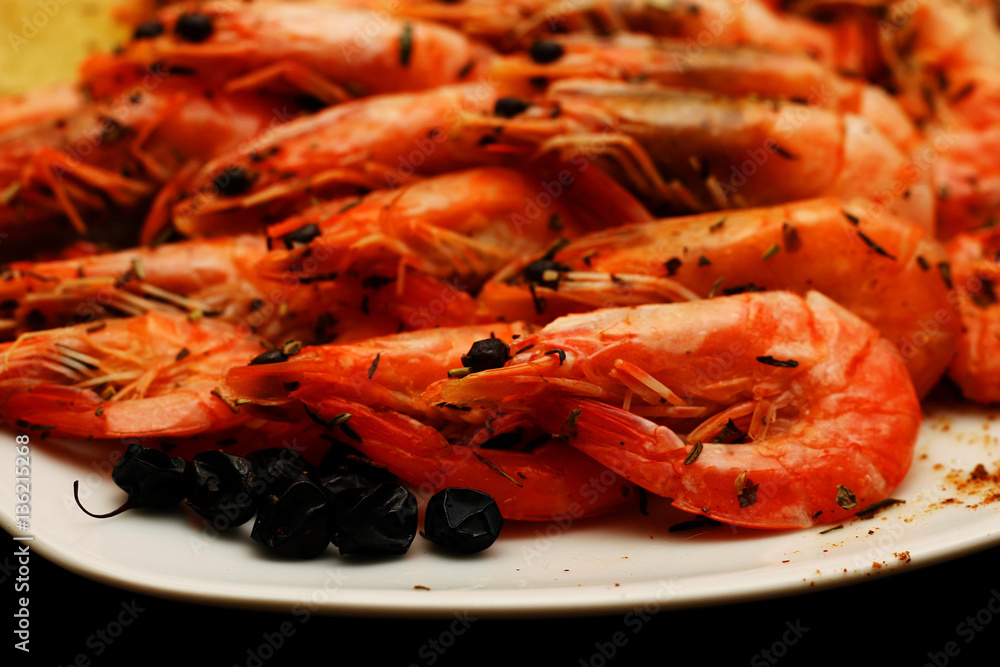 Fresh delicious hot shrimp on a white plate with spices with a lemon on a black table. Fresh delicious hot shrimp on a white plate with spices with a lemon on a black table.