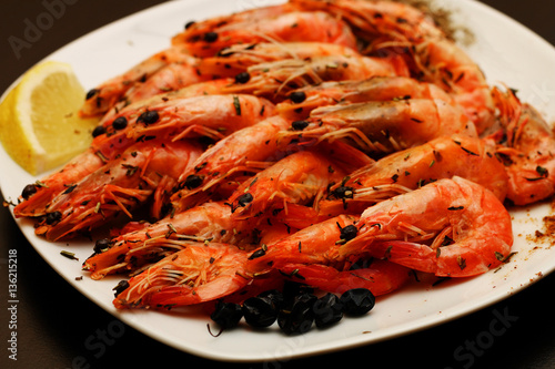 Fresh delicious hot shrimp on a white plate with spices with a lemon on a black table.