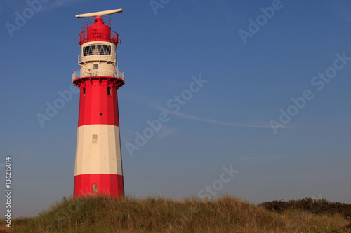 red and white striped lighthouse at sunset time in dune landscape