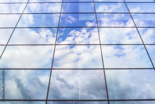 Modern glass front of building reflecting clouds and blue skies.