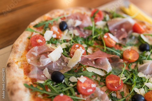 Closeup detail of Pizza with prosciutto, cherry tomatoes, grana padano cheese and rucola.
