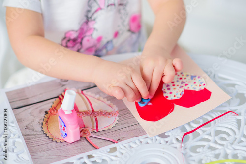 girl glues heart. She makes paper postcard.