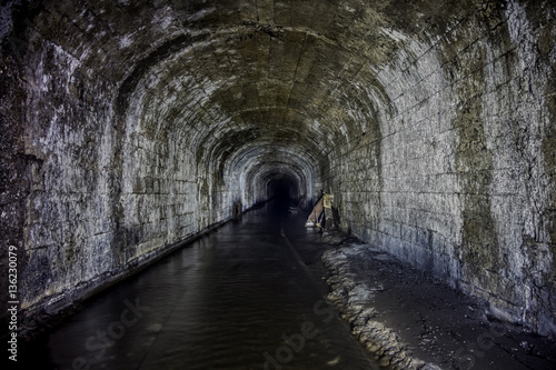 Flooded tunnel of an old abandoned coal mine with rusty remnants of railroad 