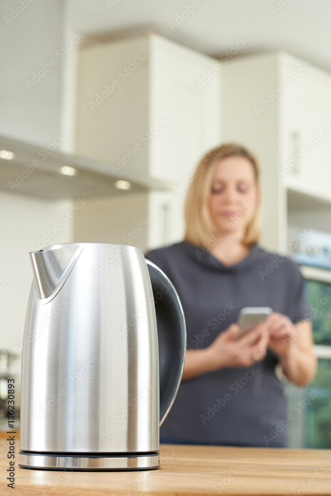 Woman Controlling Smart Kettle Using App On Mobile Phone Woman Controlling Smart Kettle Using App On Mobile Phone