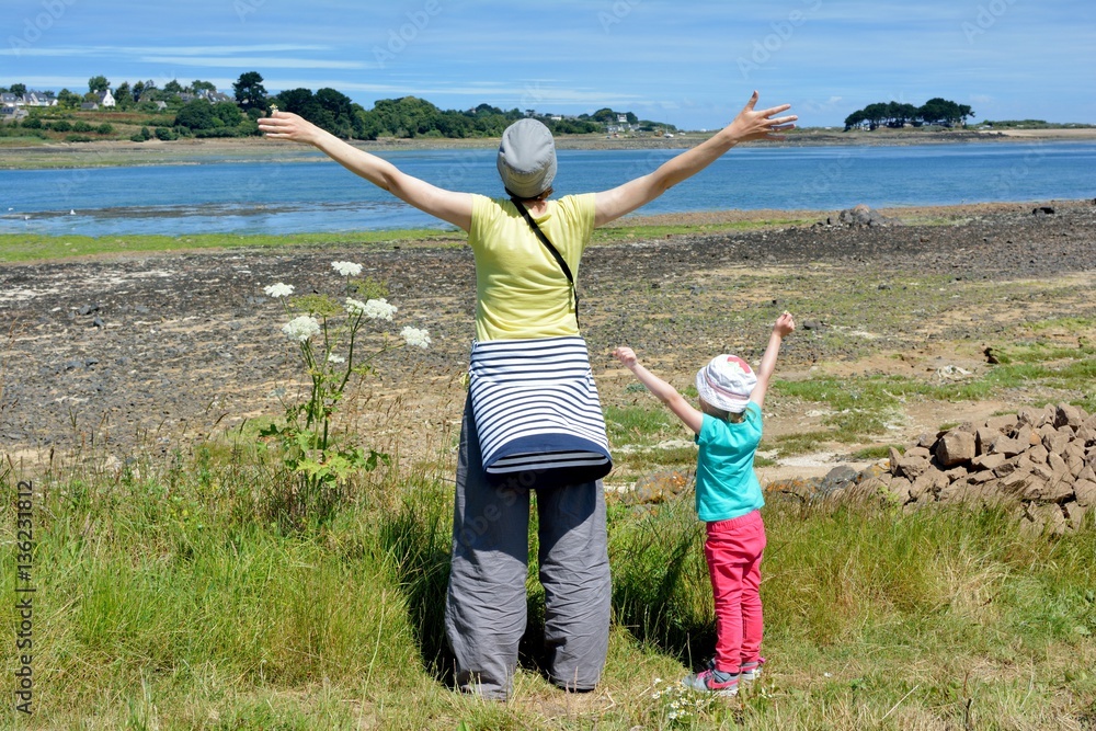Fototapeta premium Une mère et sa fille expriment leur joie les bras en l'air face à la mer