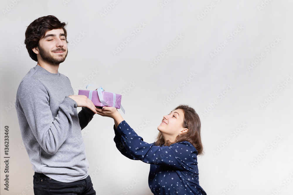 Feelings and relationships concept. A smiling young woman giving a present to her boyfriend. A pleased bearded hipster with closed eyes being pleased to receive a present from his lover Feelings and relationships concept. A smiling young woman giving a present to her boyfriend. A pleased bearded hipster with closed eyes being pleased to receive a present from his lover
