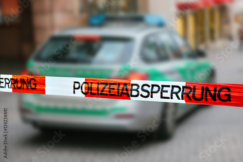 Police tape at the crime scene. Focus on the police tape, a police car on blurred background. german police. 
