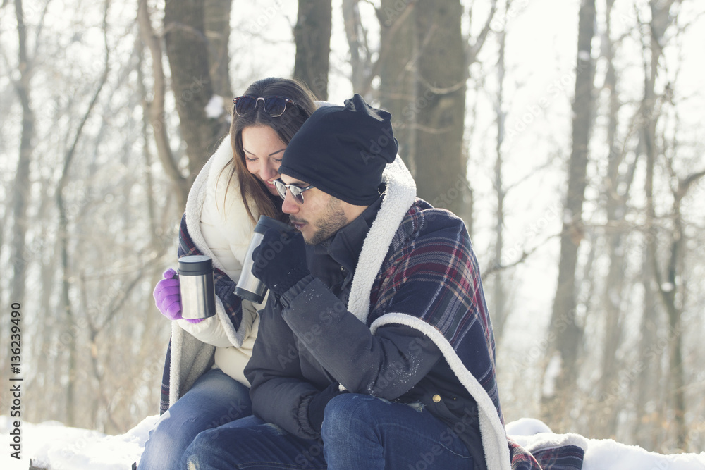 Young couple on snow with blanket and mug on hands Young couple on snow with blanket and mug on hands