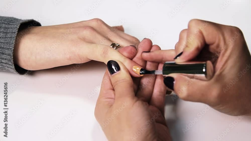 Female beautitian hand applying transparent polish on nails in beauty saloon, close up white table Female beautitian hand applying transparent polish on nails in beauty saloon, close up white table